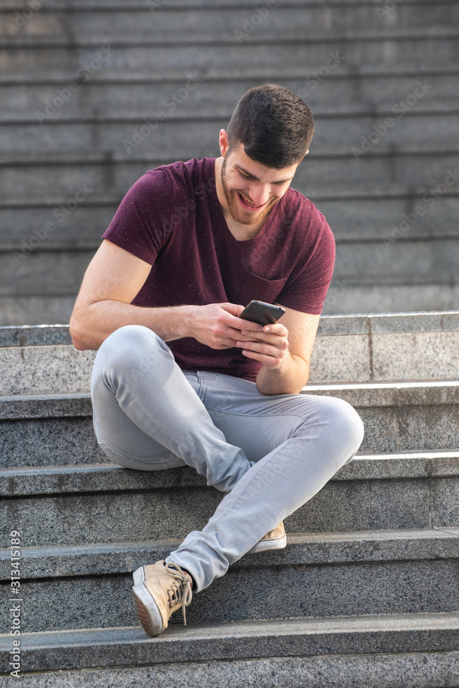 young man sitting on steps outside and looking at mobile phone