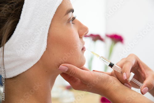 Powiększenie ust kwasem hialuronowym. Twarz kobiety podczas zabiegu modelowania ust. Kosmetolog wstrzykuje wypełniacz, medycyna estetyczna.  photo