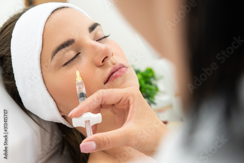 Redukcja zmarszczek zastrzykiem z kwasu hialuronowego. Twarz kobiety podczas zabiegu wolumetrii twarzy. Kosmetolog wstrzykuje wypełniacz pod oczy, medycyna estetyczna. photo