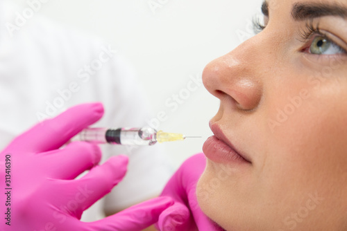 Powiększenie ust kwasem hialuronowym. Zbliżenie na usta kobiety podczas zabiegu modelowania ust. Kosmetolog wstrzykuje wypełniacz, medycyna estetyczna. 