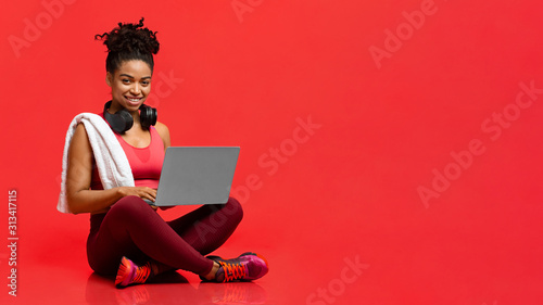 Smiling sporty athletic woman using laptop over red background