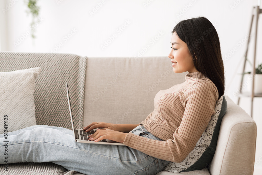 Asian freelancer girl working online on laptop, side view Asian freelancer girl working online on laptop, side view