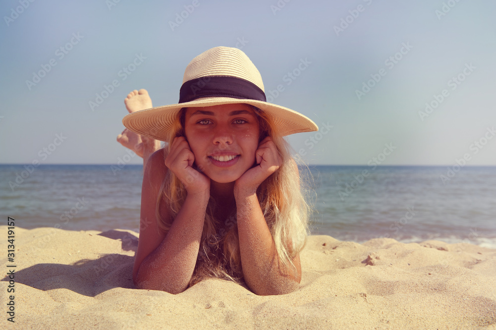 The girl in the hat lies on the beach near the sea.