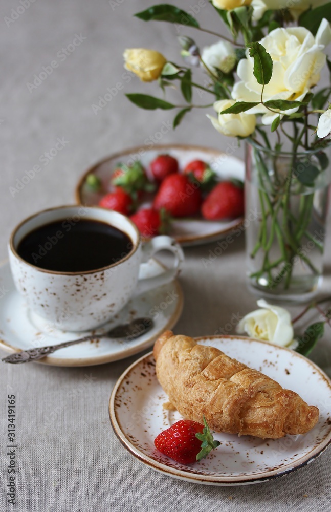 Breakfast in French. Croissant and strawberry. And black coffee, a bouquet of flowers. Fresh strawberries. Soft focus. Space for text Breakfast in French. Croissant and strawberry. And black coffee, a bouquet of flowers. Fresh strawberries. Soft focus. Space for text