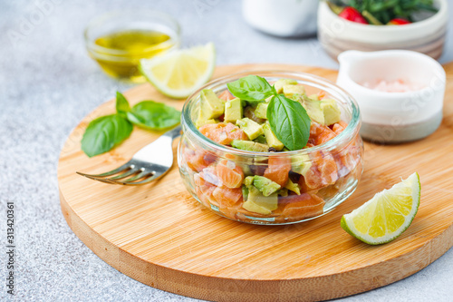 Delicious avocado and raw salmon salad, tartare, served glass jar with lime, light background photo