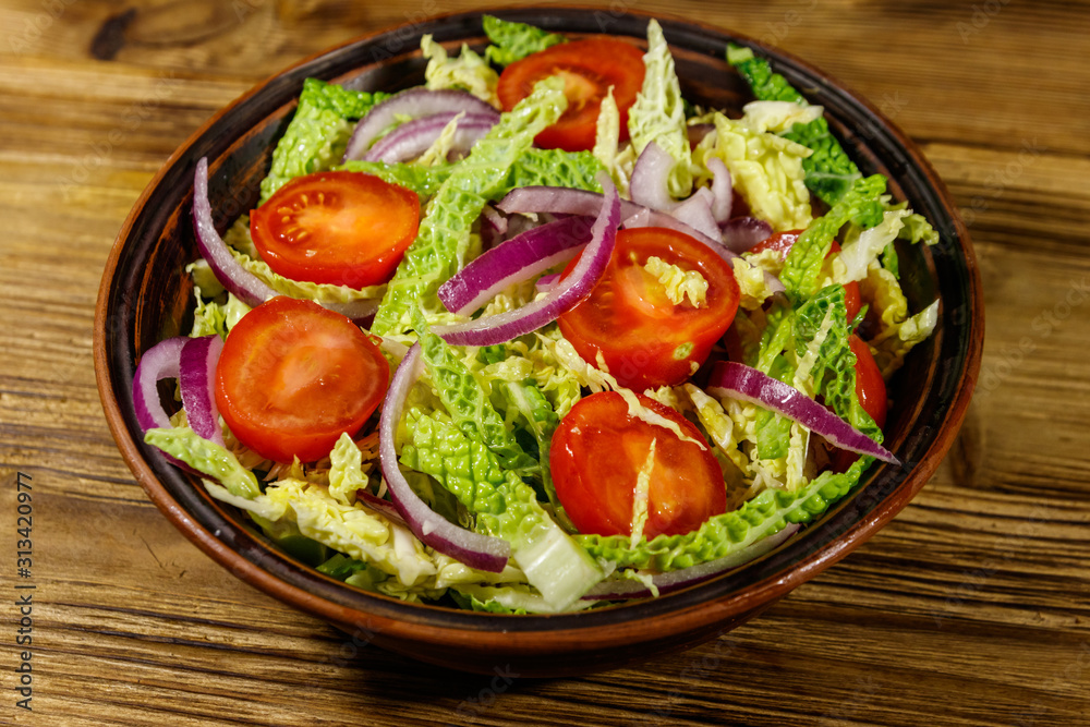 Healthy salad with savoy cabbage, cherry tomato, red onion and olive oil on wooden table