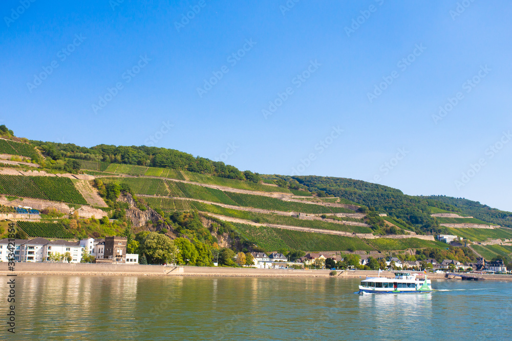 Beautiful scenic German landscape of village and tiered vineyard along the Rhine River with river cruise ship in view.