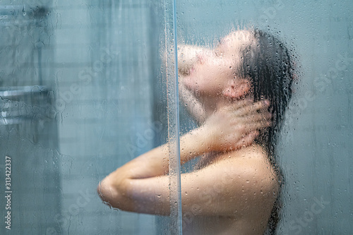 Fototapeta Young unfocused naked woman taking shower and bathing in morning shower under refreshing water jet through the bath screen with little drops
