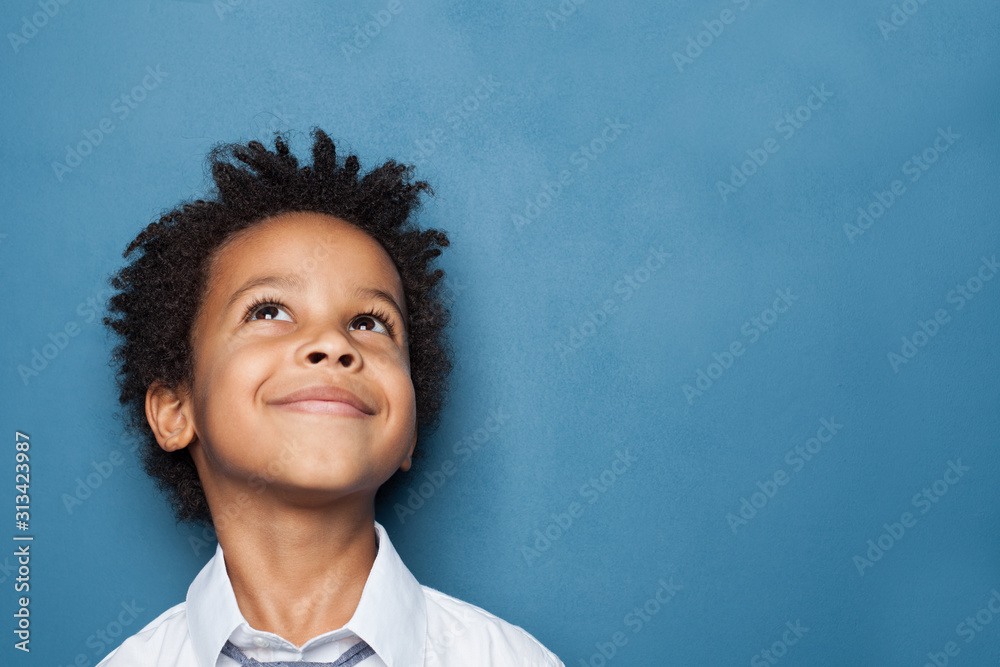 Little black child boy smiling and looking up on blue background - obrazy, fototapety, plakaty 