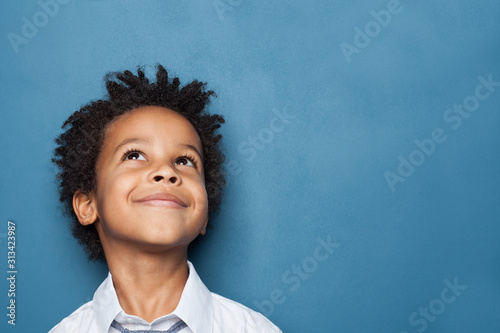 Fotótapéta Little black child boy smiling and looking up on blue background