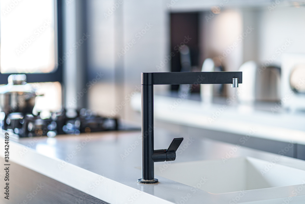 Fototapeta premium Black kitchen faucet with a white sink in a stylish modern kitchen