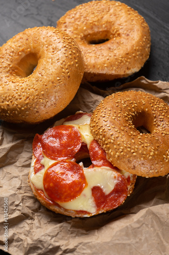 Sesame bagels with pepperoni and cheese on dark background