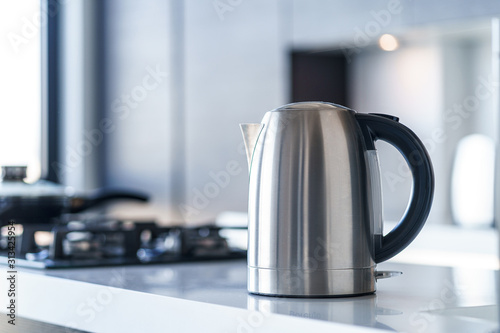 Silver metal electric kettle for boiling water and making tea on a table in the kitchen interior. Household kitchen appliances for makes hot drinks photo