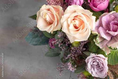 bright bouquet of different varieties of roses with a rosette of brassica on a gray background. horizontal image  copy space