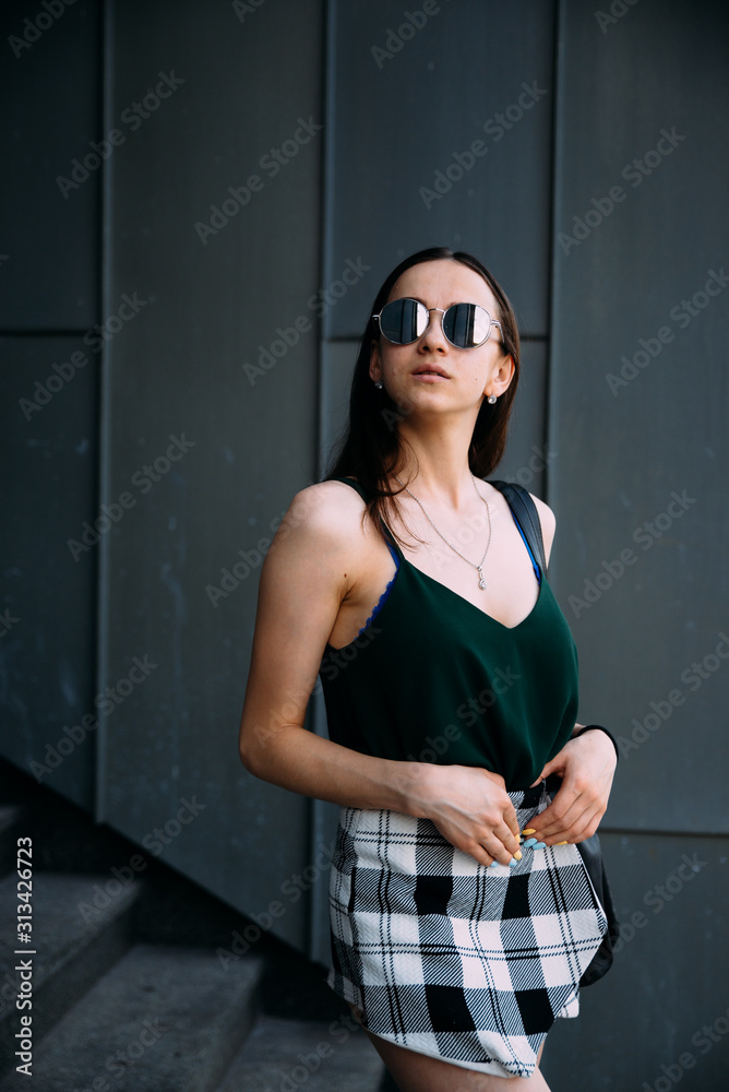 Obraz premium Sexy girl near a dark wall in a T-shirt, sunglasses and short shorts