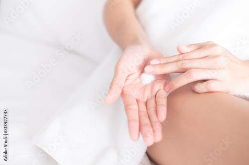 Woman applying moisturizing cream/lotion on hands on white bed, beauty concept...