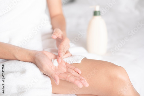 Woman applying moisturizing cream/lotion on hands on white bed, beauty concept...