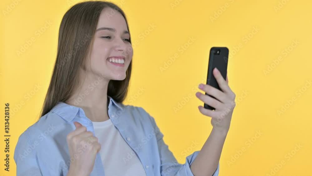 Casual Young Woman Celebrating on Smartphone, Yellow Background Casual Young Woman Celebrating on Smartphone, Yellow Background