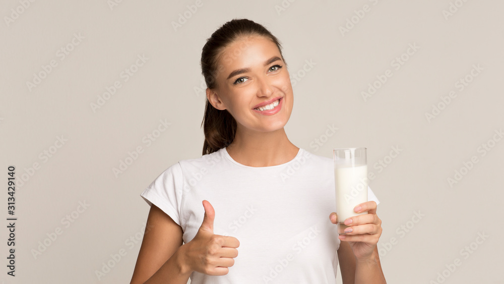 Woman Holding Glass Of Milk Gesturing Thumbs-Up Standing In Studio Woman Holding Glass Of Milk Gesturing Thumbs-Up Standing In Studio