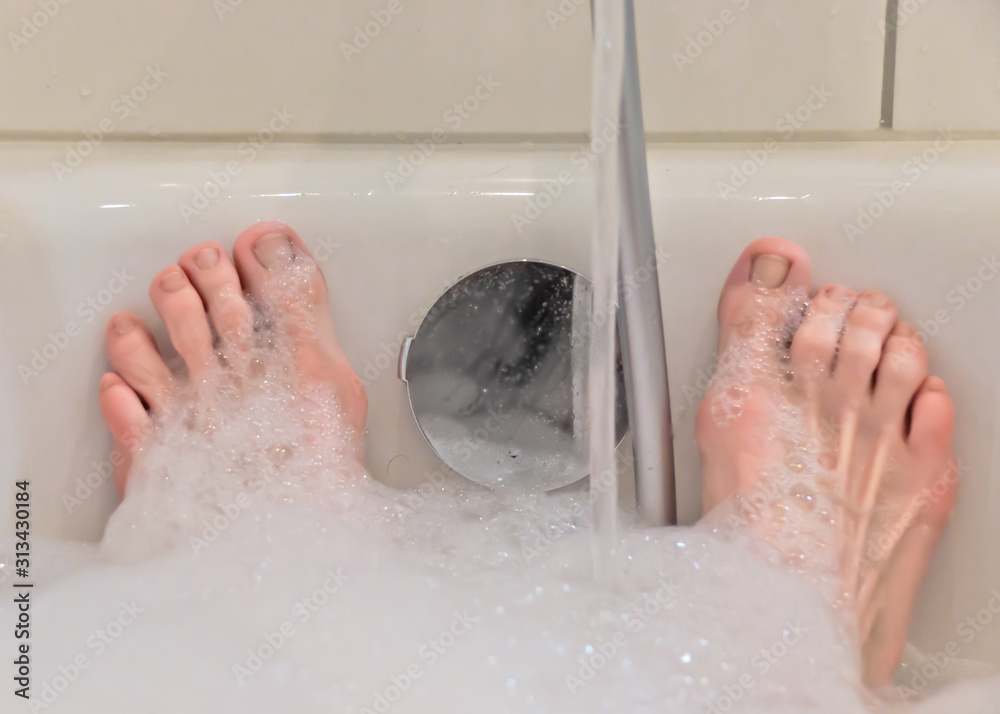 A bathtub in a bathroom filled with warm water and foam, only the feet of a person are showed