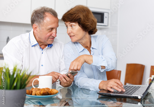 Mature man and woman using smartphone and  working at laptop