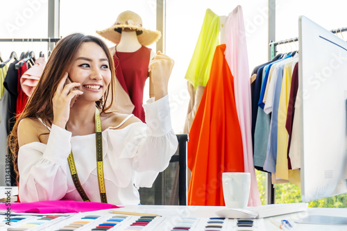 Beautiful young designer woman work with computer tailer fabric fashion small business with smilling and happiness while receive order from smartphone. Business start up and entrepreneur owner concept photo