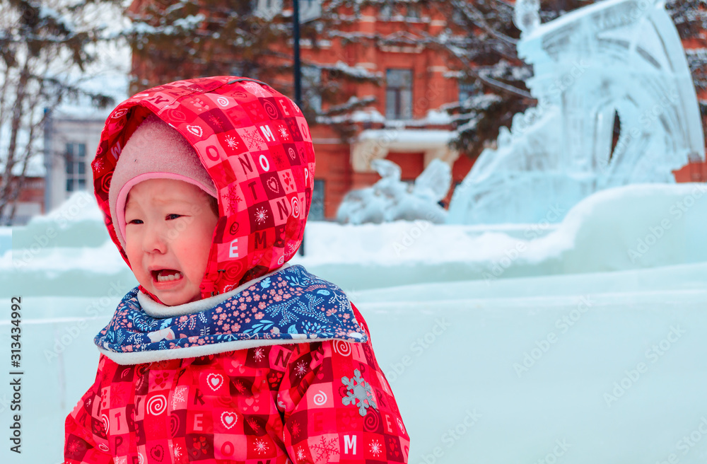 Cute Asian little girl in pink colorful jumpsuit portrait crying on white fluffy snow in the Park. an unhappy child on the street in the snow on a cold winter day.