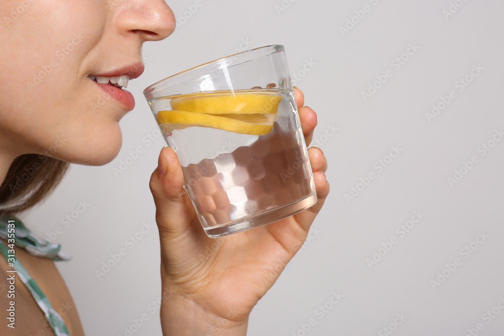 Young woman drinking lemon water on light background, closeup Young woman drinking lemon water on light background, closeup
