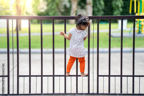 Little girl climbing on metal fence.