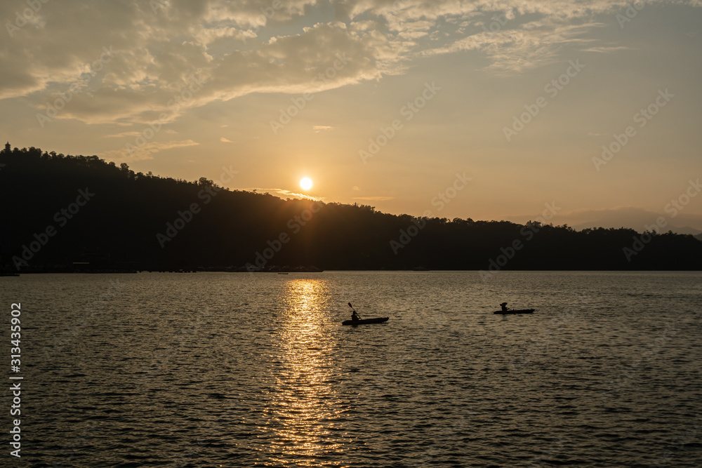 Traveller canoeing on lake during sunset.