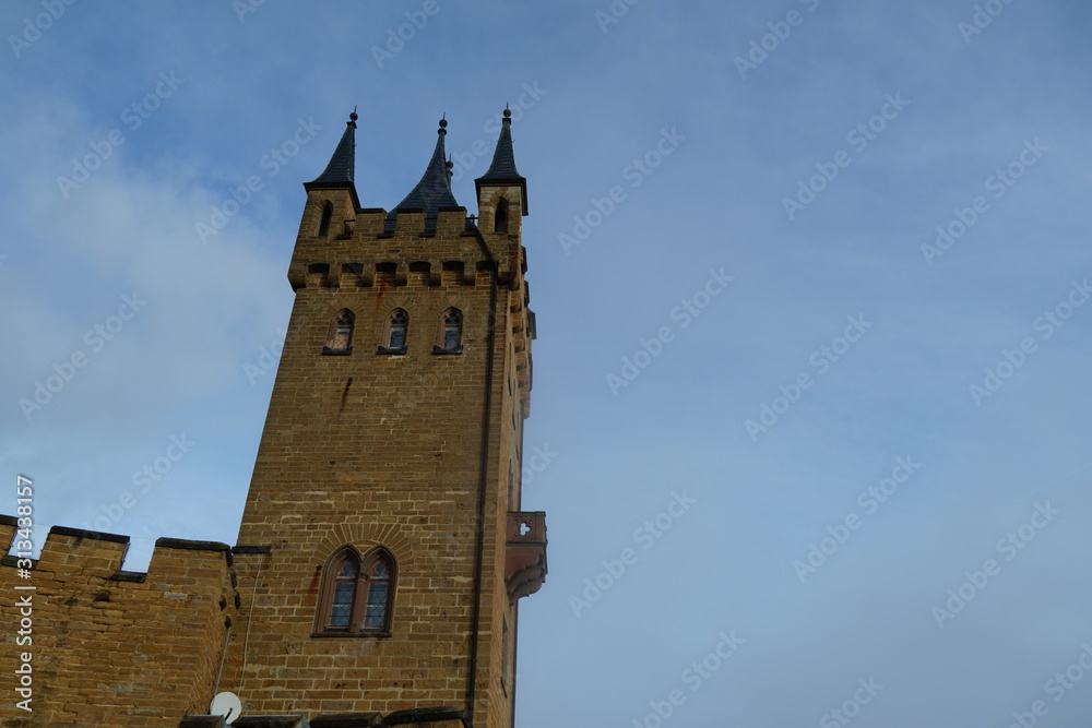 Tower of Hohenzollern castle with a balcony and three window. Photo taken from an upward perspective on the background of the sky with thin white clouds