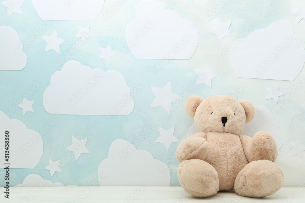 Teddy bear on white wooden table near wall with blue sky, space for text. Baby room interior - obrazy, fototapety, plakaty 