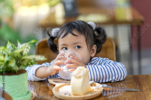 Cute little girl enjoy eating cake at wooden table.