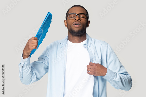 Obraz na płótnie African guy waving fan cooling in hot weather studio shot