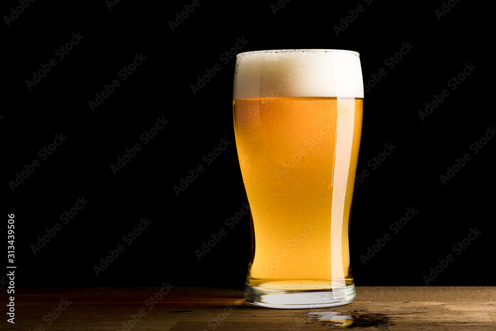 Beer in glass, spilled on wooden table, isolated on black background, copy space