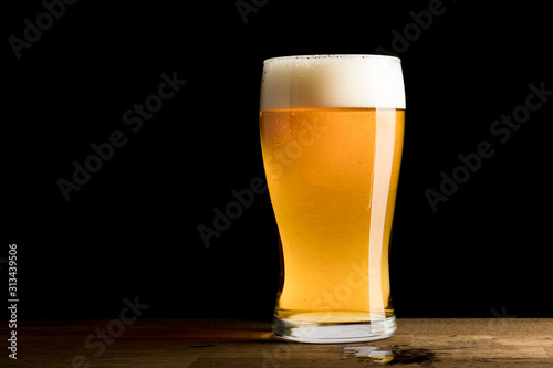 Beer in glass, spilled on wooden table, isolated on black background, copy space