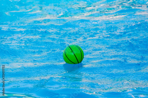 Green ball on the water in the pool in sunny weather_