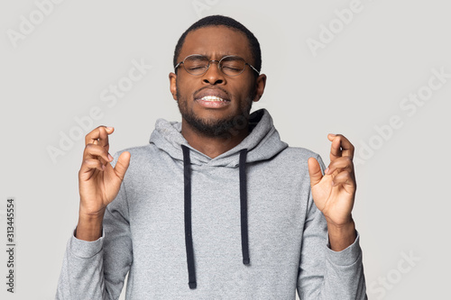 Konstfotografi Superstitious african guy closed eyes crossing fingers wishing good luck