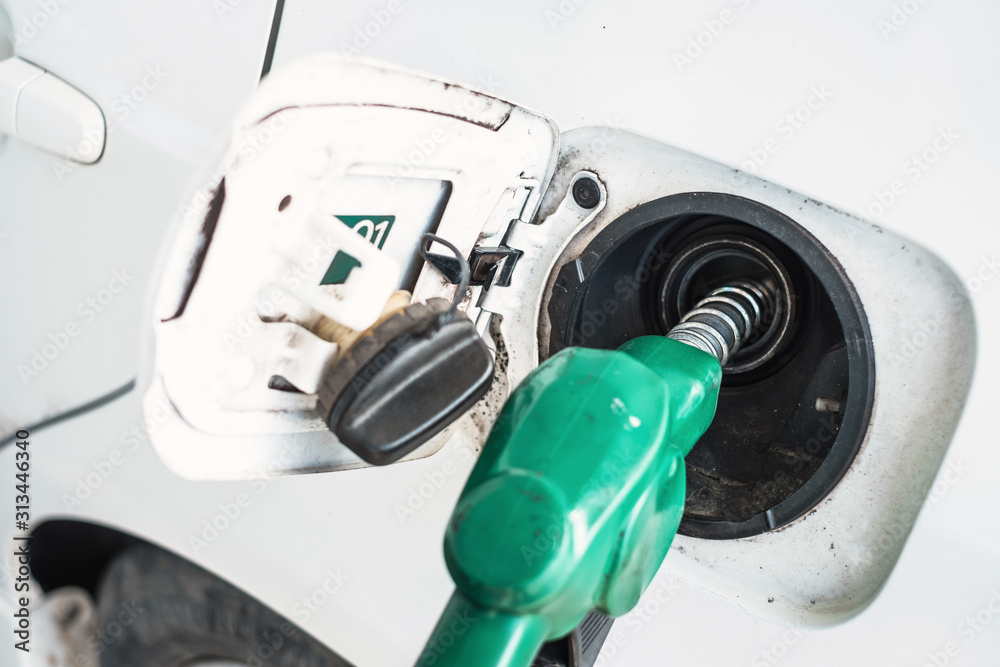 Close up of green gas refueling gun refueling gas into a white car at a gas station Close up of green gas refueling gun refueling gas into a white car at a gas station