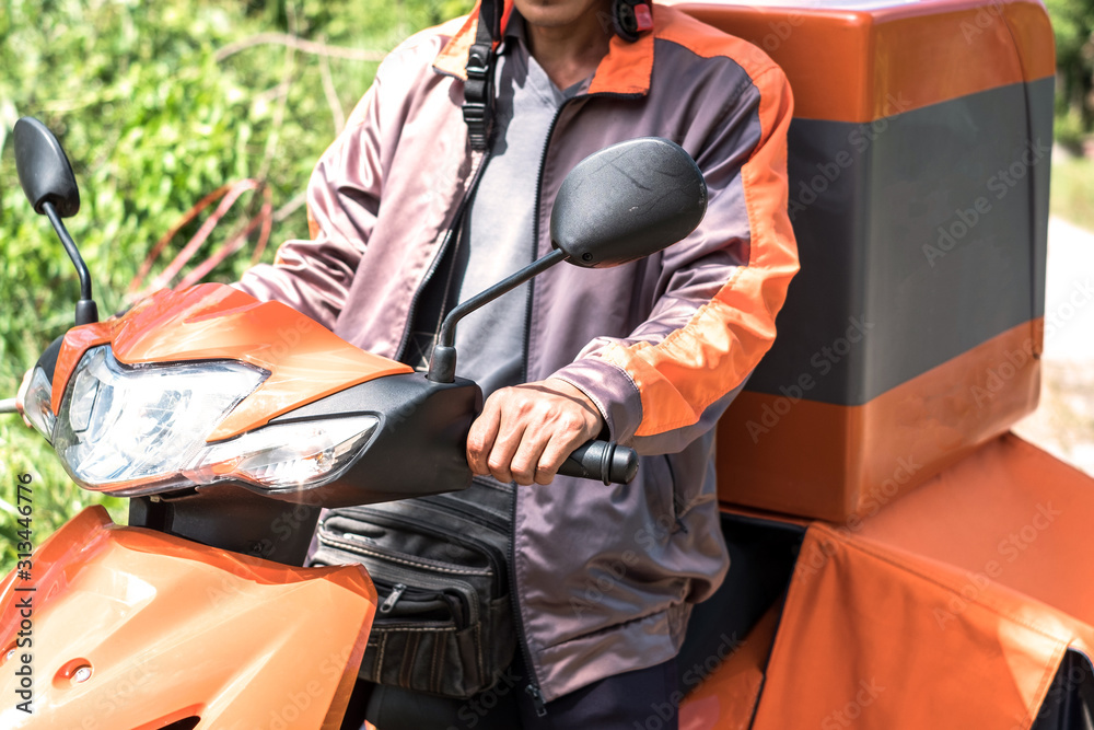 Selective focus at hand of delivery man in orange uniform using motorcycle to delivery parcel. Selective focus at hand of delivery man in orange uniform using motorcycle to delivery parcel.