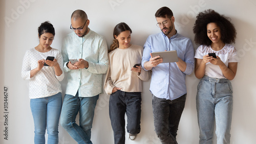Fotografie Multiracial young people stand using diverse electronic gadgets