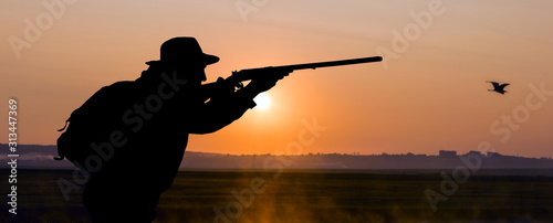 Silhouette of a hunter on the background of the morning red dawn. Stands at the ready with a gun.