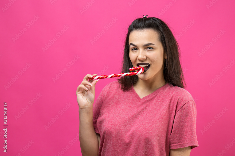 Portrait of lovely sweet beautiful cheerful woman with straight brown hair trying to bite red candy cane christmas.