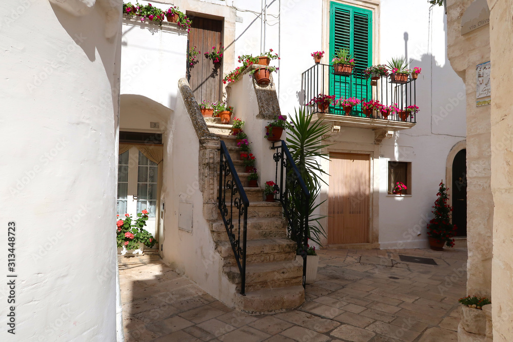 Fototapeta premium Street in Locorotondo town, Italy, region of Apulia, Adriatic Sea - entrance to the houses with stairway and balcony full of flowers