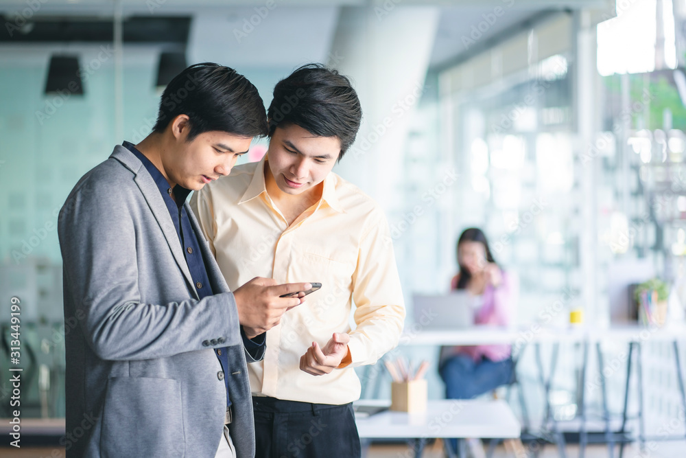 Young Asian businessmen using a smartphone and digital notebook to discuss information in a modern business working space. Young Asian businessmen using a smartphone and digital notebook to discuss information in a modern business working space.