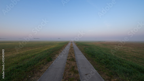 Field path through meadows covered with fog during sunrise © Thomas