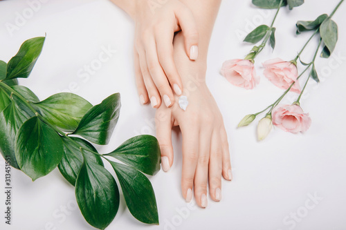 Concept spa skin care. Top view cosmetic cream on female hands with pink flowers on white background, flat lay