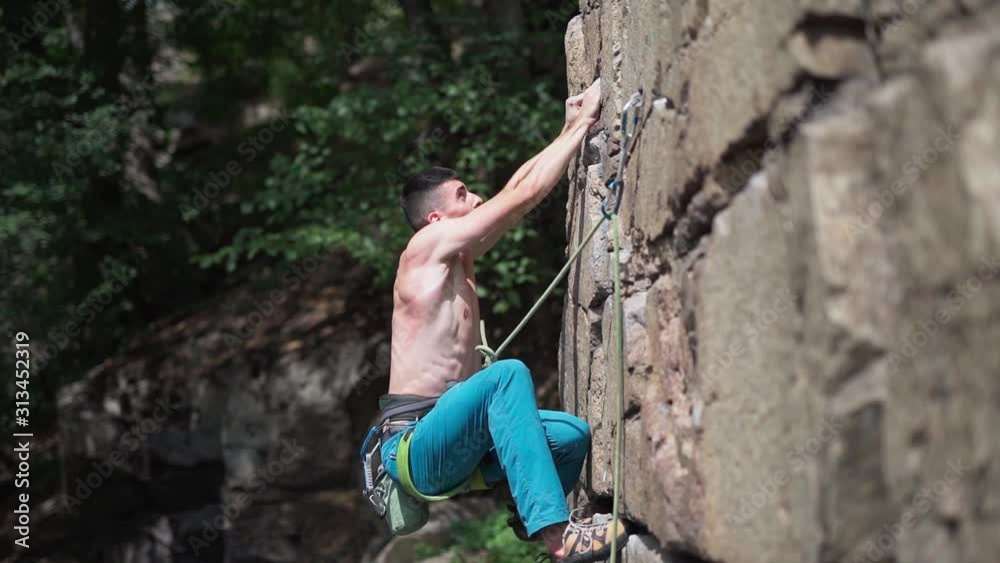 young man rock climber with naked torso climbs on a granite cliff, gripping hold but fulling. summer outdoors rock climbing and active lifestyle concept, slow motion FullHD stock footage