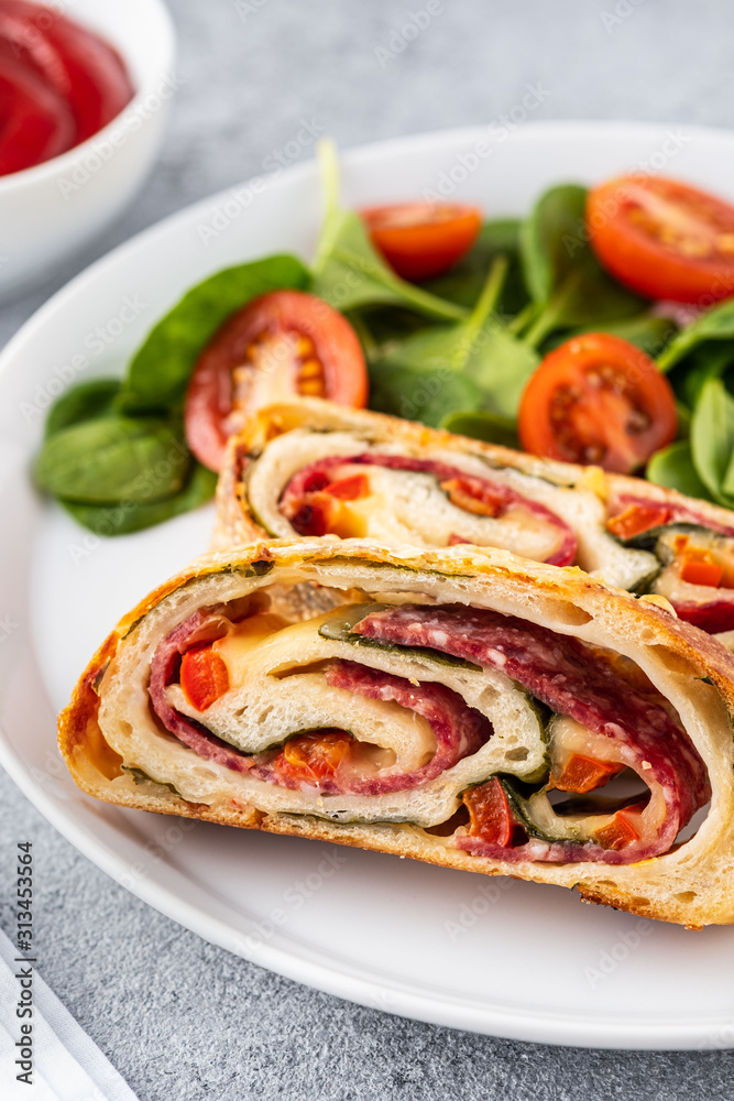 Italian food Pizza roll stromboli with cheese, salami, spinach and red pepper a light background. Italian food Pizza roll stromboli with cheese, salami, spinach and red pepper a light background.