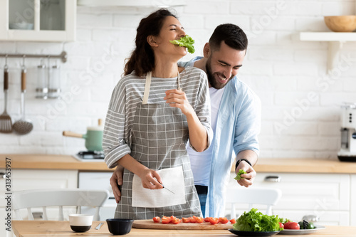 Couple preparing healthy vegetarian salad laughing enjoying process in kitchen